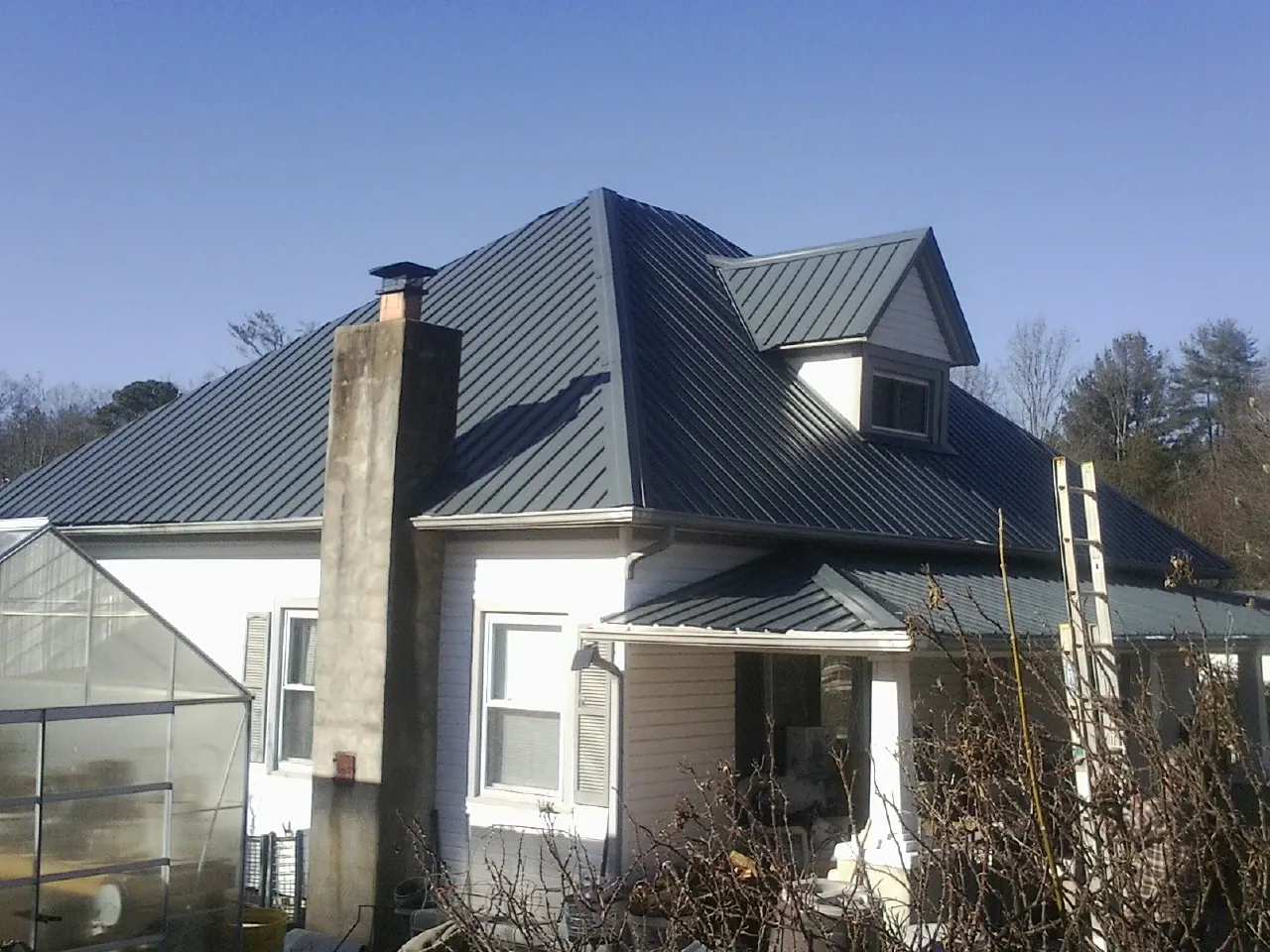 Dark blue standing seam metal roof on a white farmhouse with dormer — Slate & Tile Roof Repair by Roofing Brothers in Swisher