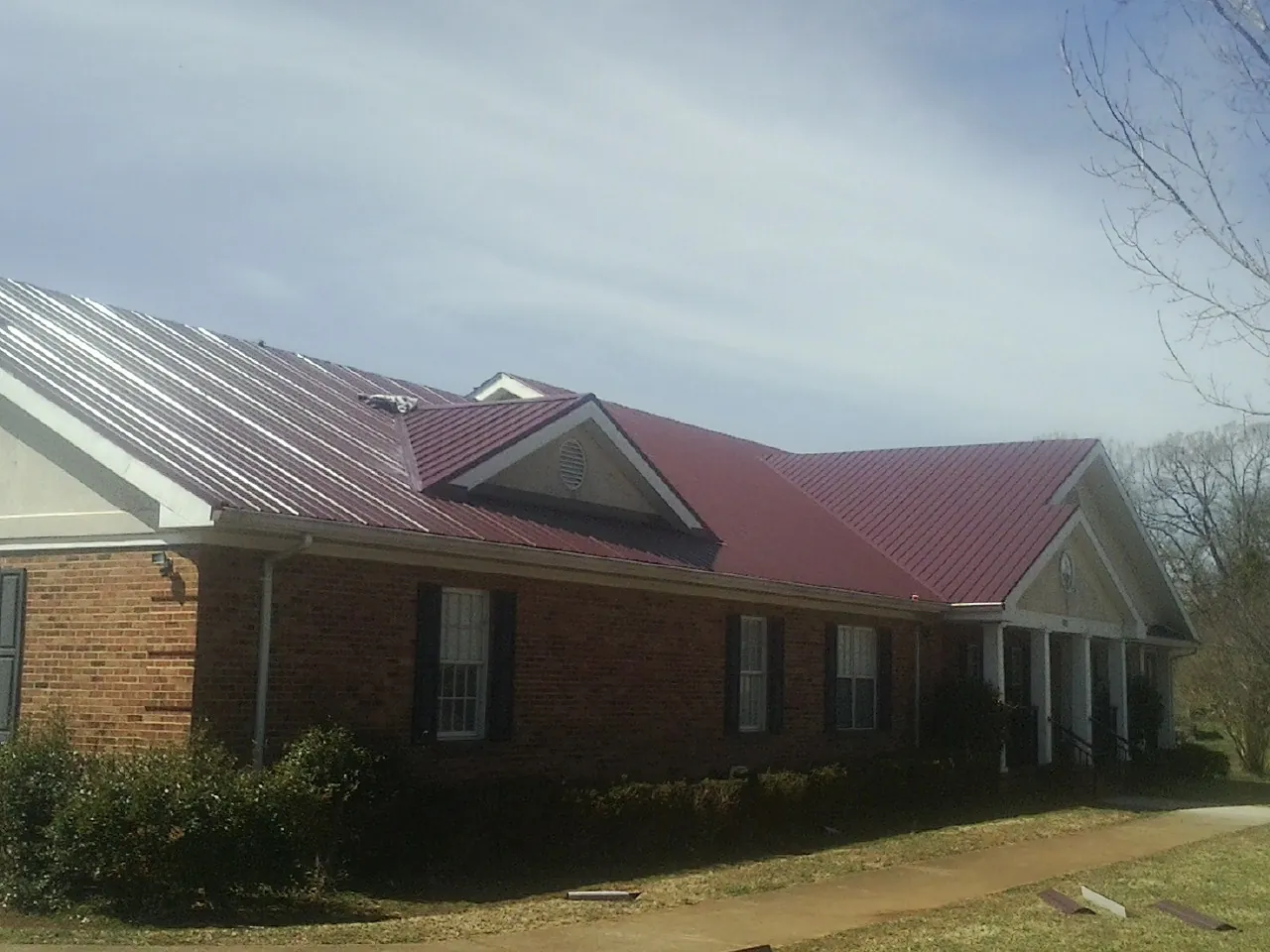 Red metal roof with gabled entries on a long brick building, from a Hail Damage Roof Repair job in Swisher