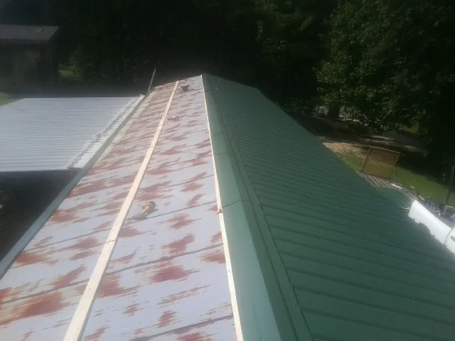 Old rusted panels beside newly installed green metal roofing — Wind Damage Roof Repair by Roofing Brothers in Swisher