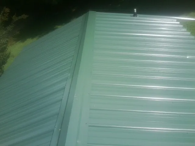 New green metal panels meeting at the ridge of a roof — Flat Roof Repair work by our crew in Swisher