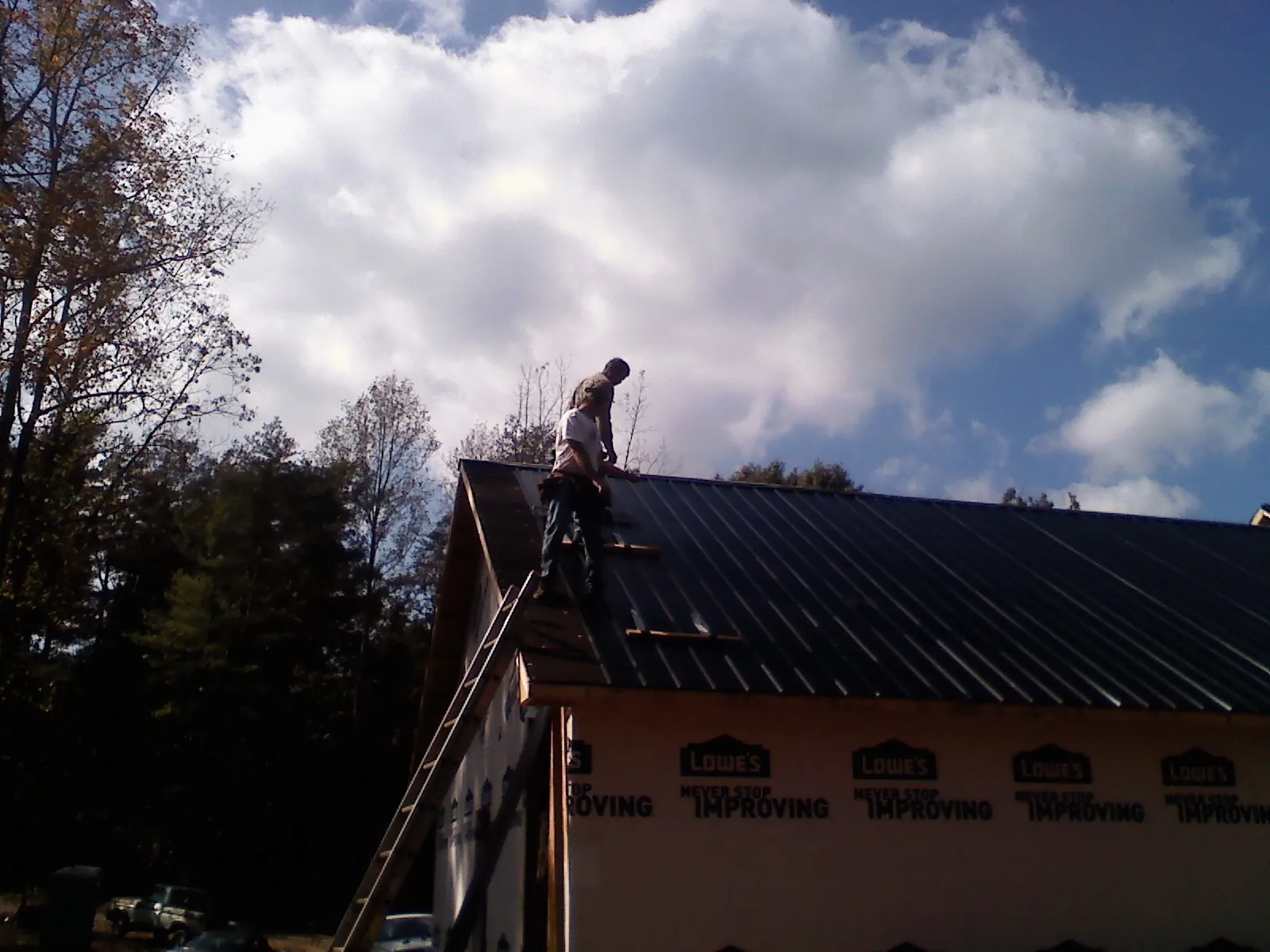 Roofer fastening dark metal panels high against a cloudy sky, from a Roof Inspection job in Swisher