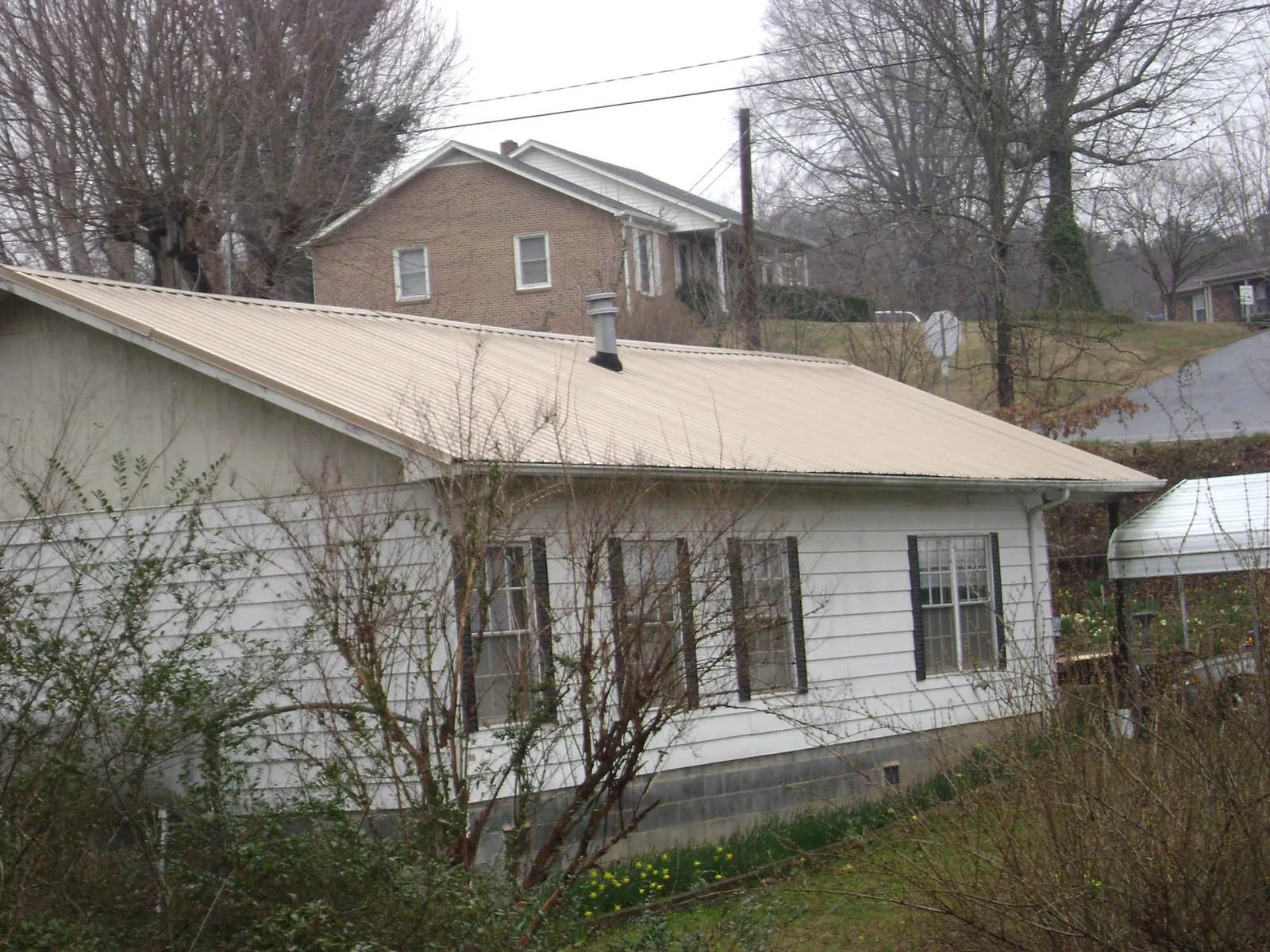 Tan metal roof on a white sided house set into a hillside — Commercial Roofing by Roofing Brothers in Swisher