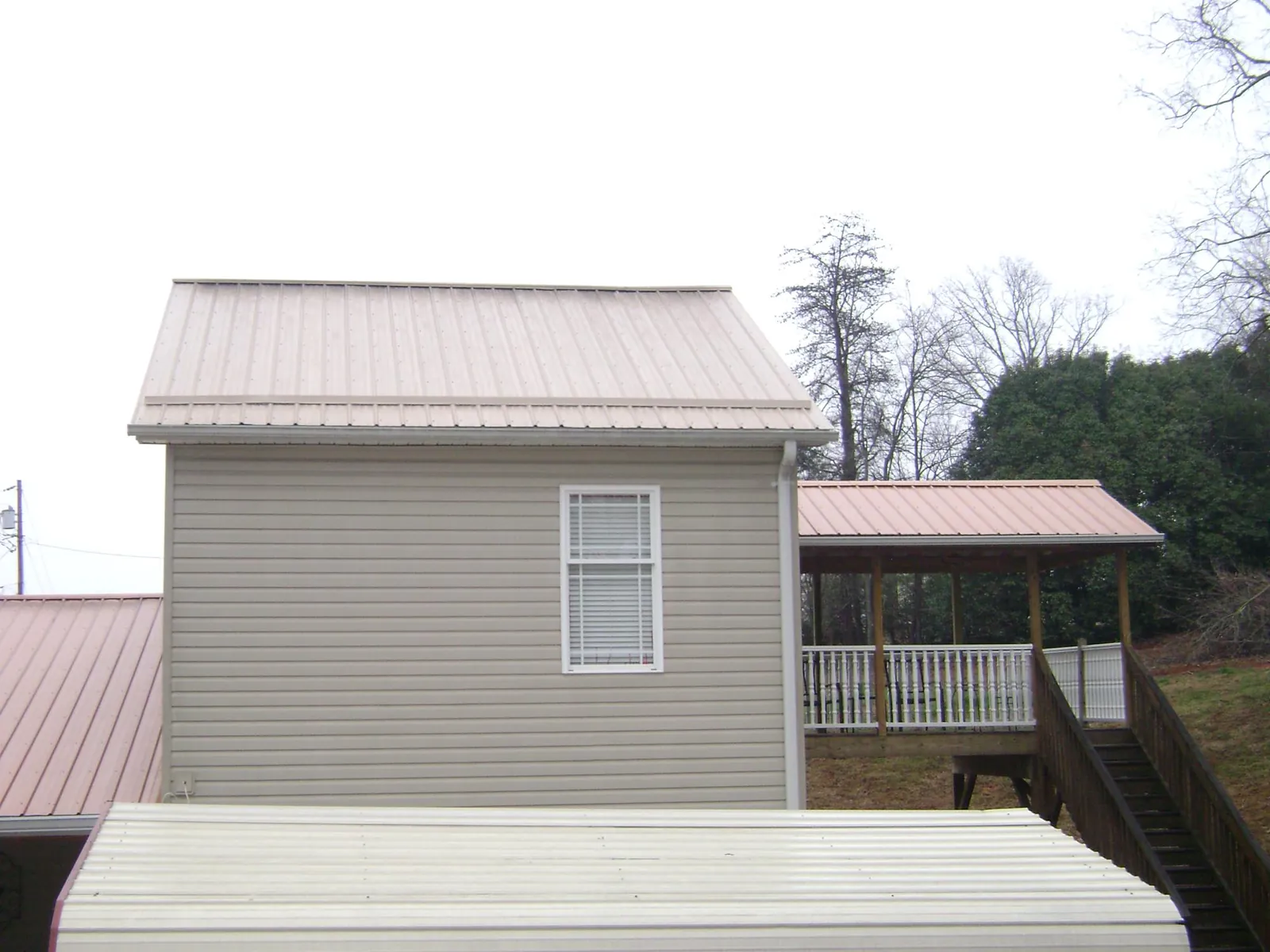 Tan metal roofs on a two story addition and attached porch, from a Roof Replacement job in Swisher